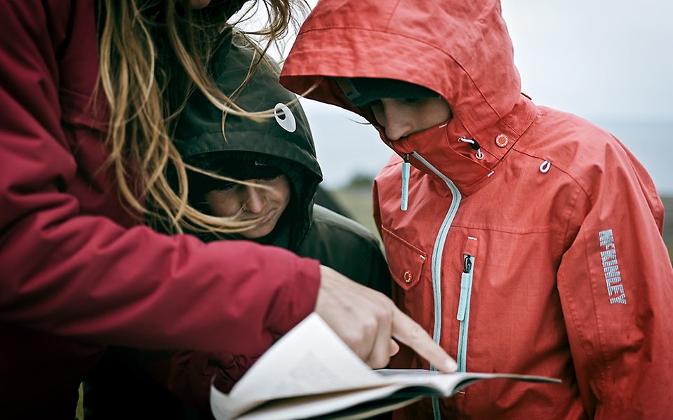 En vuxen och två barn står och tittar på en karta i regnet